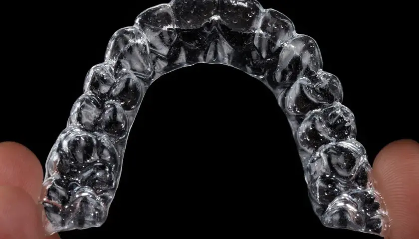 Przezroczysty aparat Invisalign, trzymany palcami, z widocznymi indywidualnymi nakładkami na zęby.