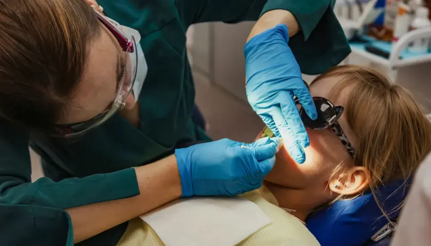 Dentystka wykonuje lakowanie zębów u dziecka. Sprawdź, jaka jest lakowanie zębów cena i zadbaj o uśmiech swojej pociechy.