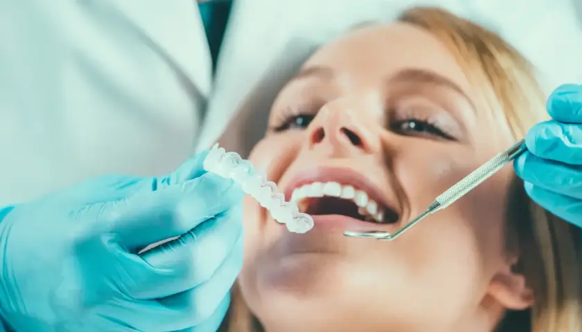 Dentysta w niebieskich rękawiczkach pokazuje pacjentce przezroczystą szynoprotezę.